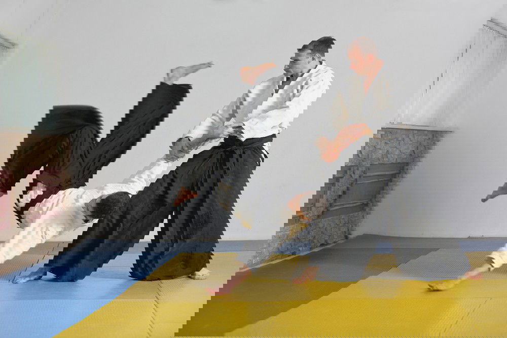 Homem sendo derrubado no chão por outro rapaz,  em uma luta de aikido.