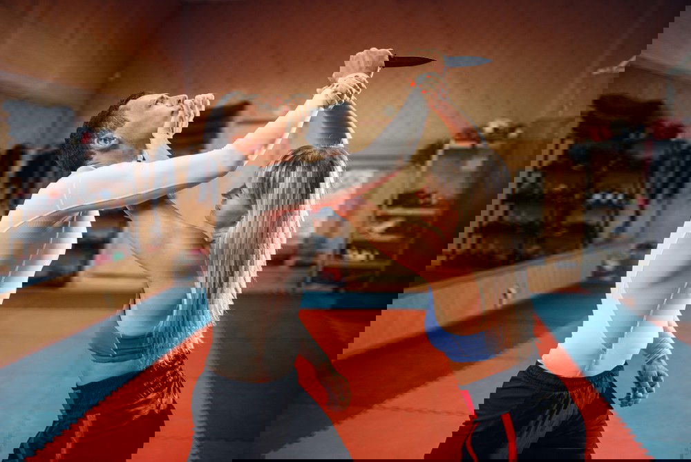 Mulher se defende de um atacante com faca, segurando seu braço e empurrando sua cabeça, em um treino de kombato.