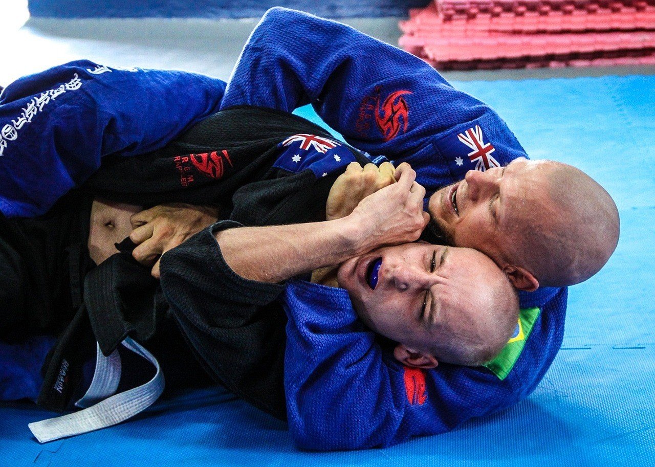 Um homem agarra o outro pelas costas durante um golpe de jiu-jítsu.