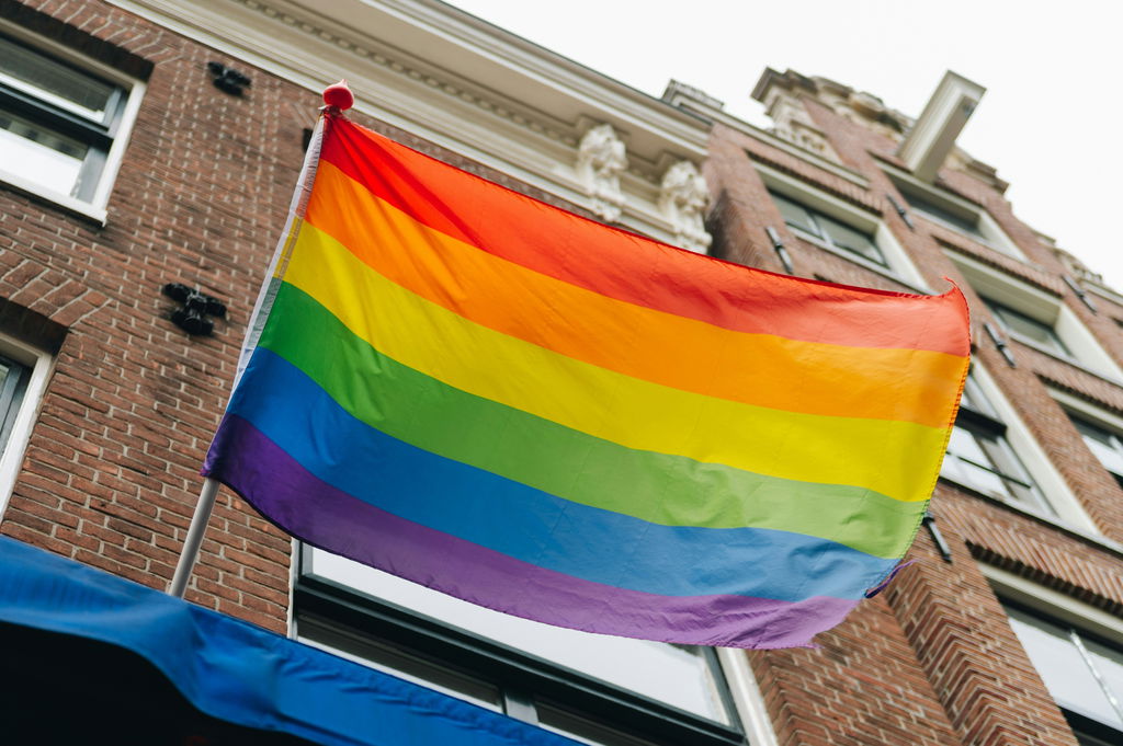 A tradicional bandeira do arco-íris da comunidade LGBTQIA+ sob o céu azul diurno.