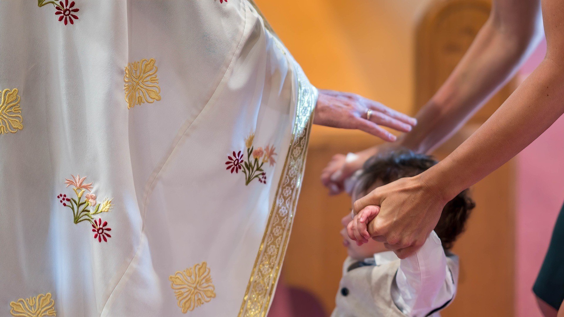 Padre católico ergue a mão sobre uma criança para abençoá-la.