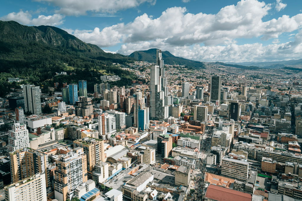 Cidade vista de cima com prédios e casas ao lado direito e uma montanha verde ao lado esquerdo.