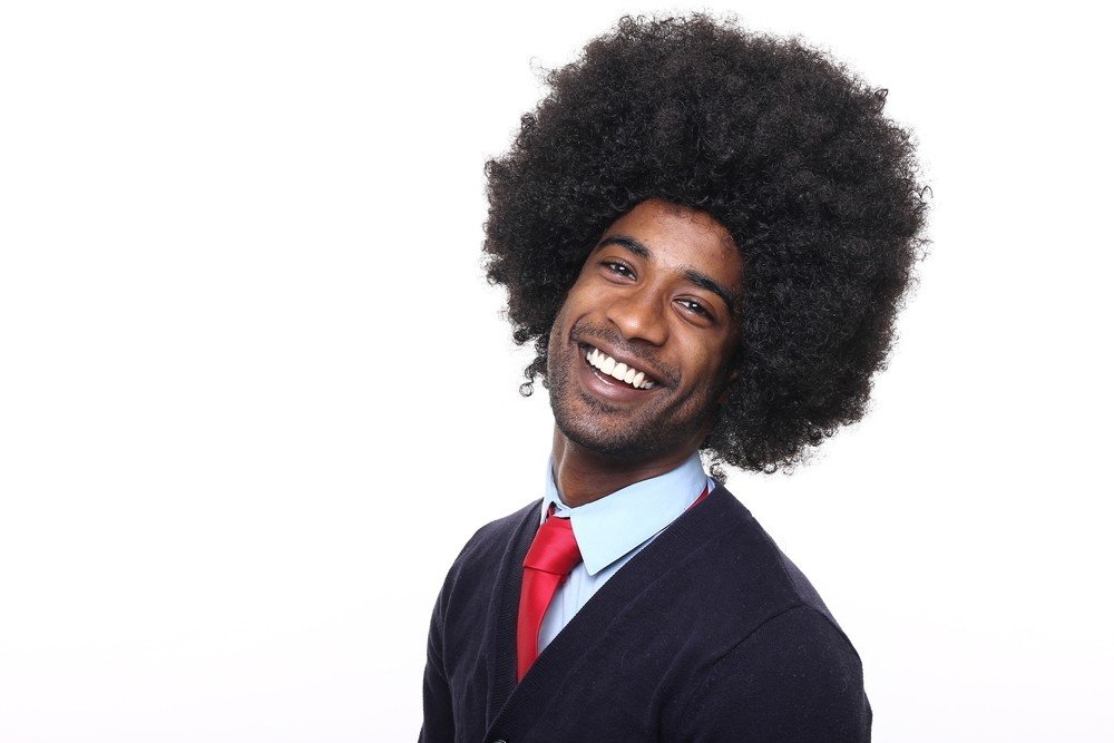 Homem negro, com cabelo back power, de terno e gravata, sorri em direção a câmera.