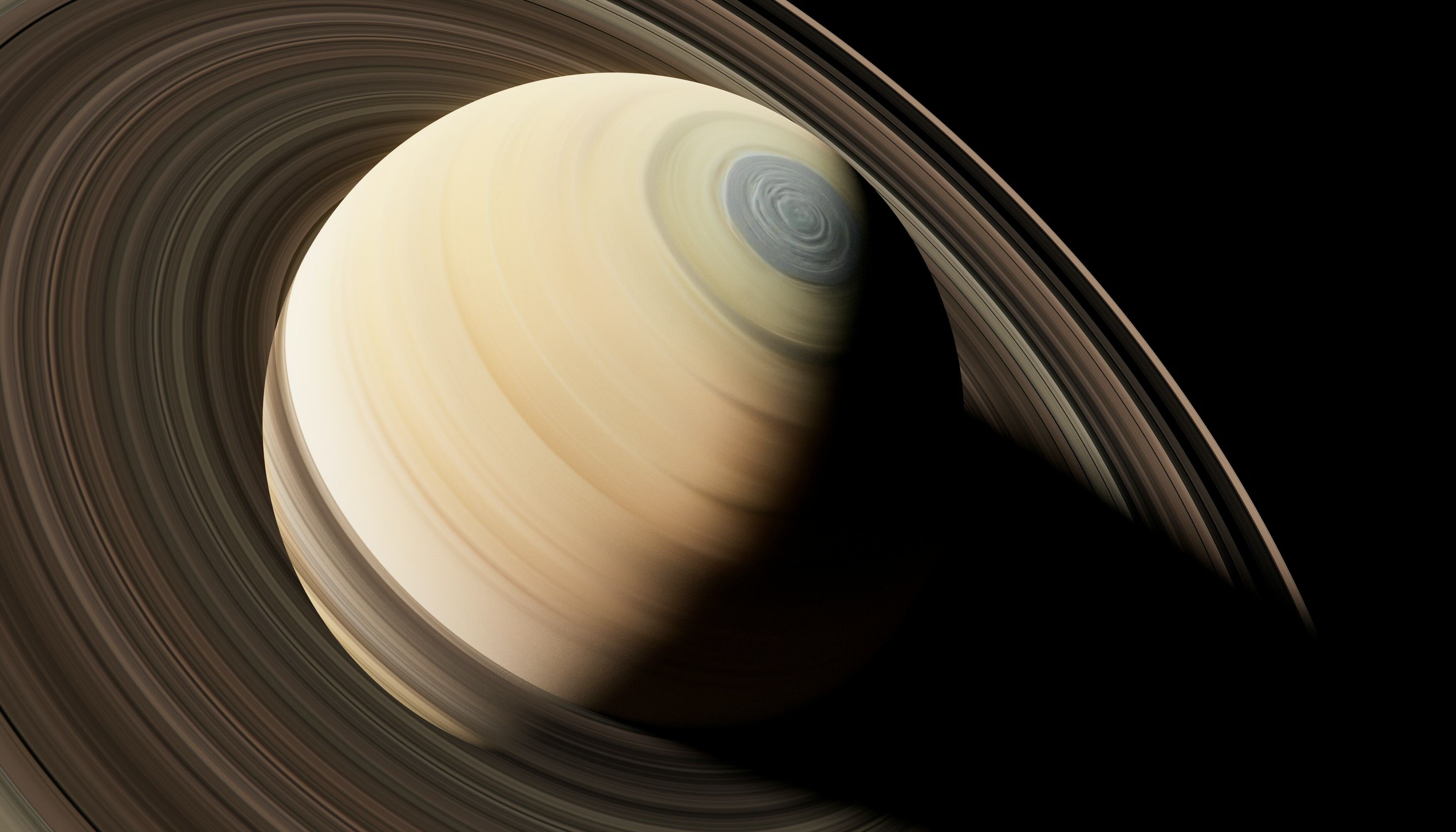 Planeta Saturno em tons amarelos, observado em diagonal com destaque para os seus anéis.