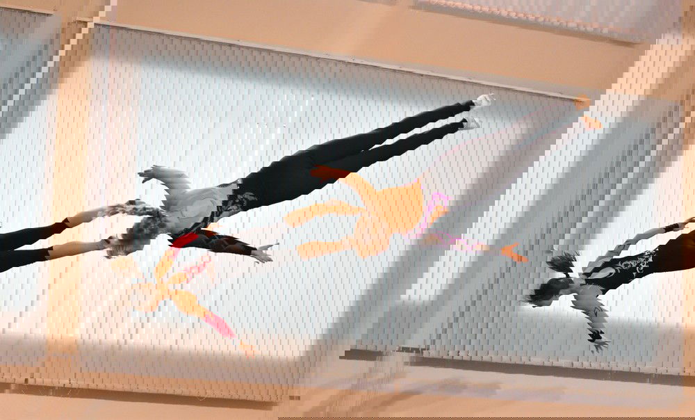 Duas ginastas de trampolim, em treinamento, suspensas no ar, com a cabeça para baixo,  após pular na cama elástica.