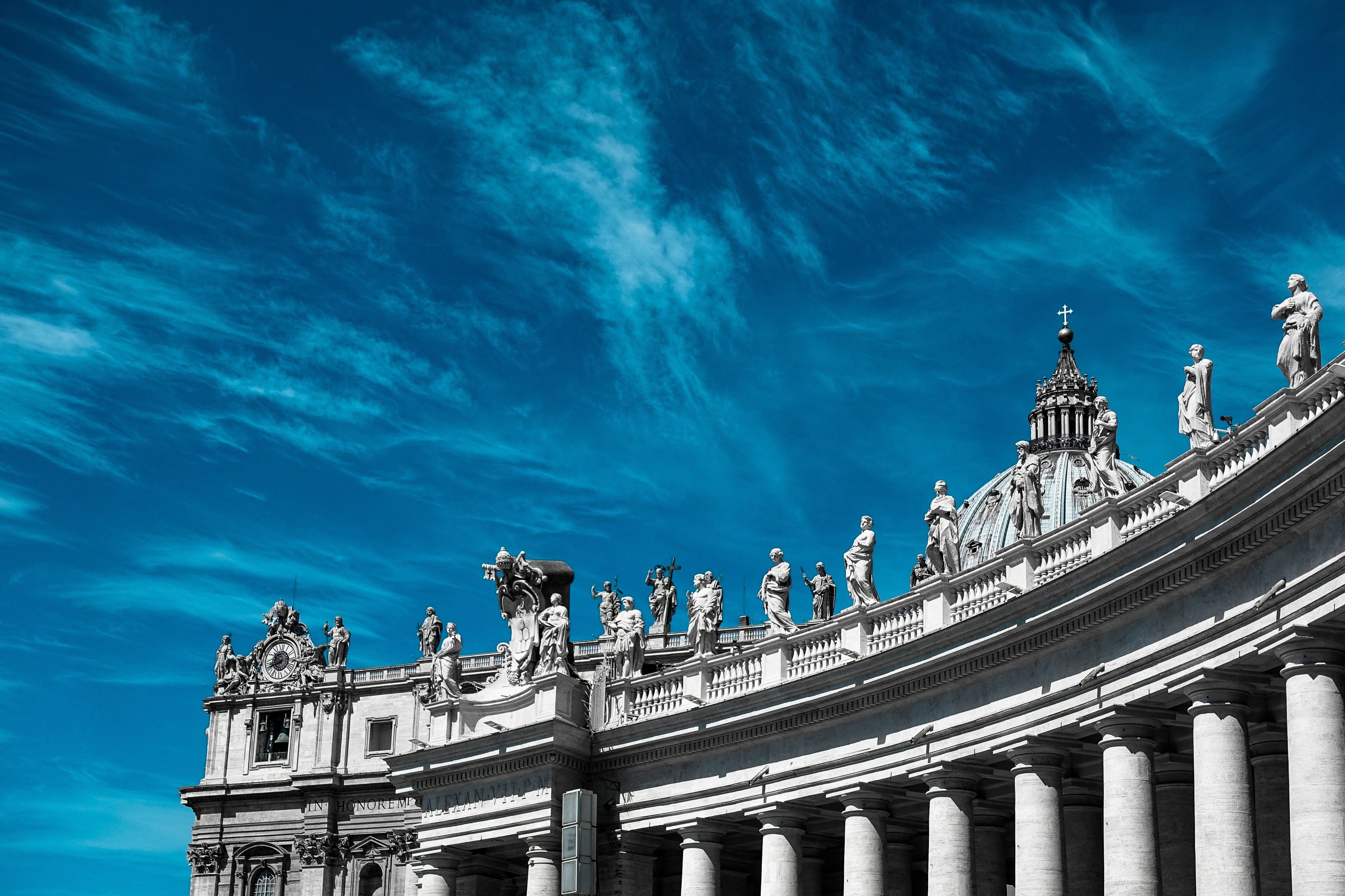 Alto da Capela de São Pedro, no Vaticano, com suas estátuas em pedra sob o céu azul diurno.