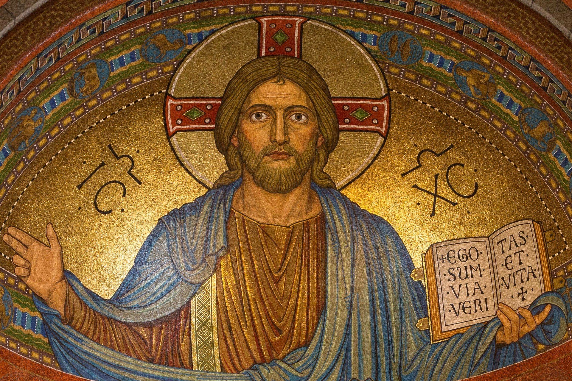 Jesus Cristo ao centro, com os braços abertos e a Bíblia na mão esquerda em tons de dourado, vermelho e azul.