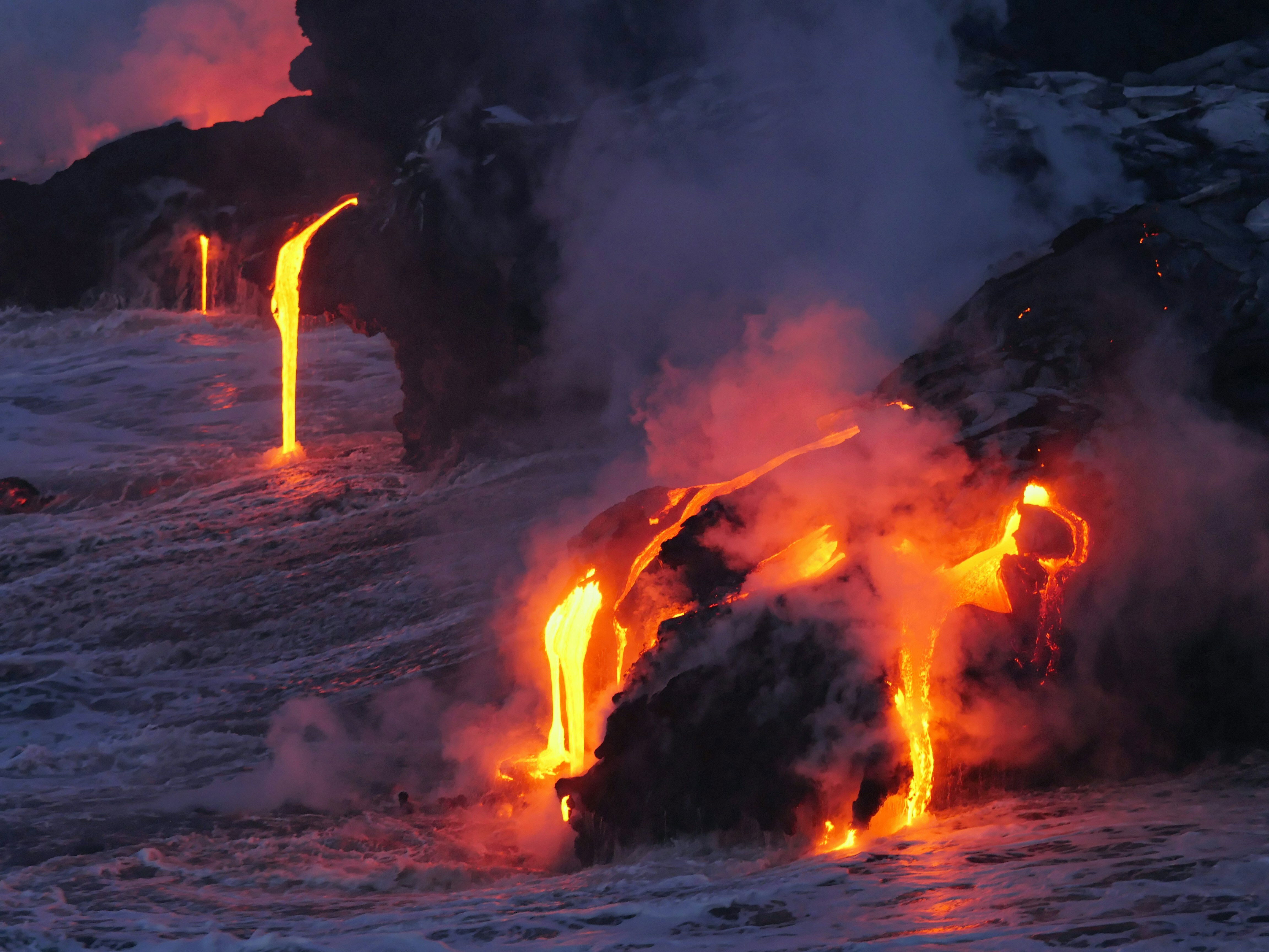 Lava de vulcão de cor alaranjada pelo forte calor cobre praia e chega ao mar de cor verde, no fim de tarde.