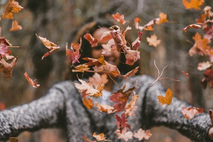 mulher joga folhas secas para o alto durante um dia de outono
