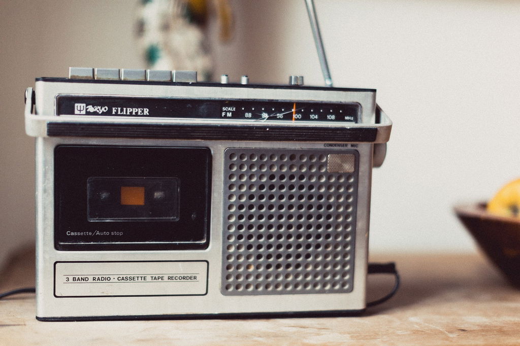 Rádio cinza com botões superiores sobre a mesa.