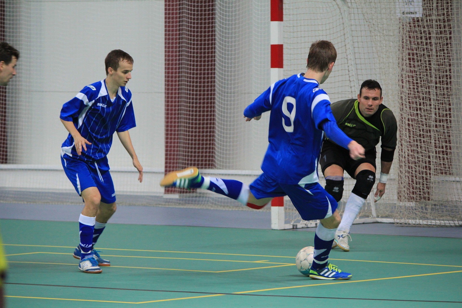 Jogador de Futsal em uniforme azul se prepara para marcar um gol em frente ao goleiro.