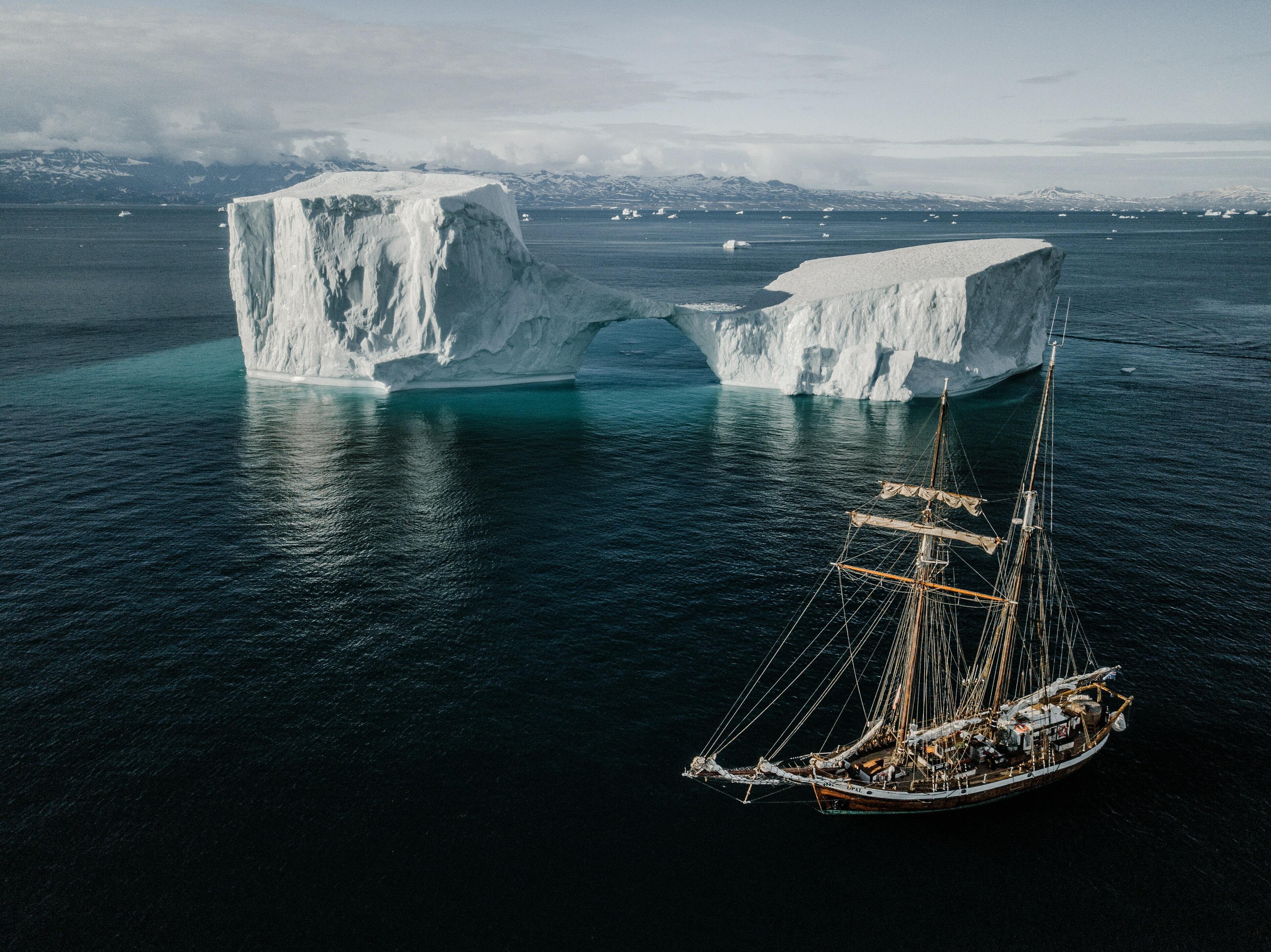 Barco circula perto de dois enormes icebergs.