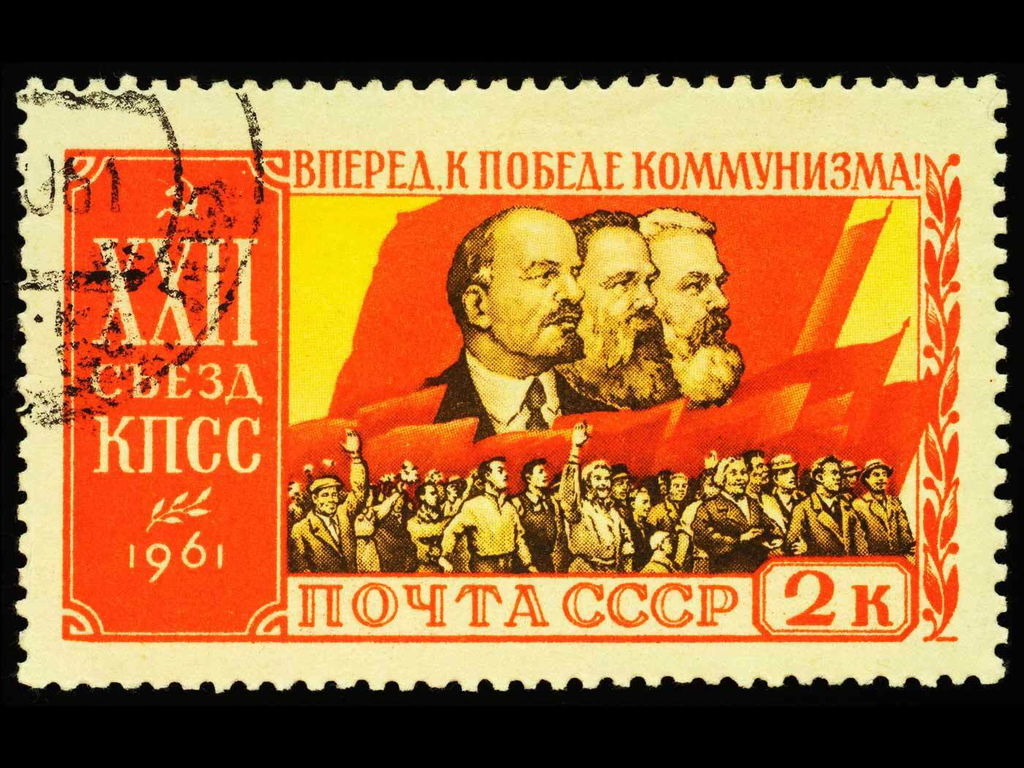Selo em tons de vermelho e amarelo que mostra os rostos de Marx, Engels e Lênin acompanhado de uma multidão de apoiantes.
