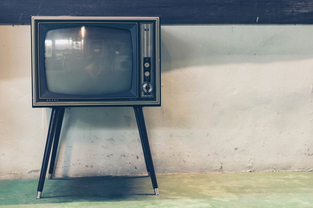 Televisão antiga de cor preta no canto esquerdo de uma parede cinzenta.